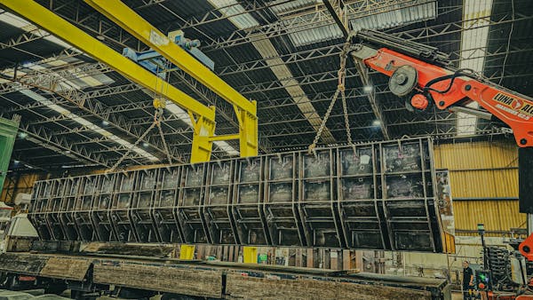 A robust industrial crane hoists a large metal container inside a spacious warehouse setting.